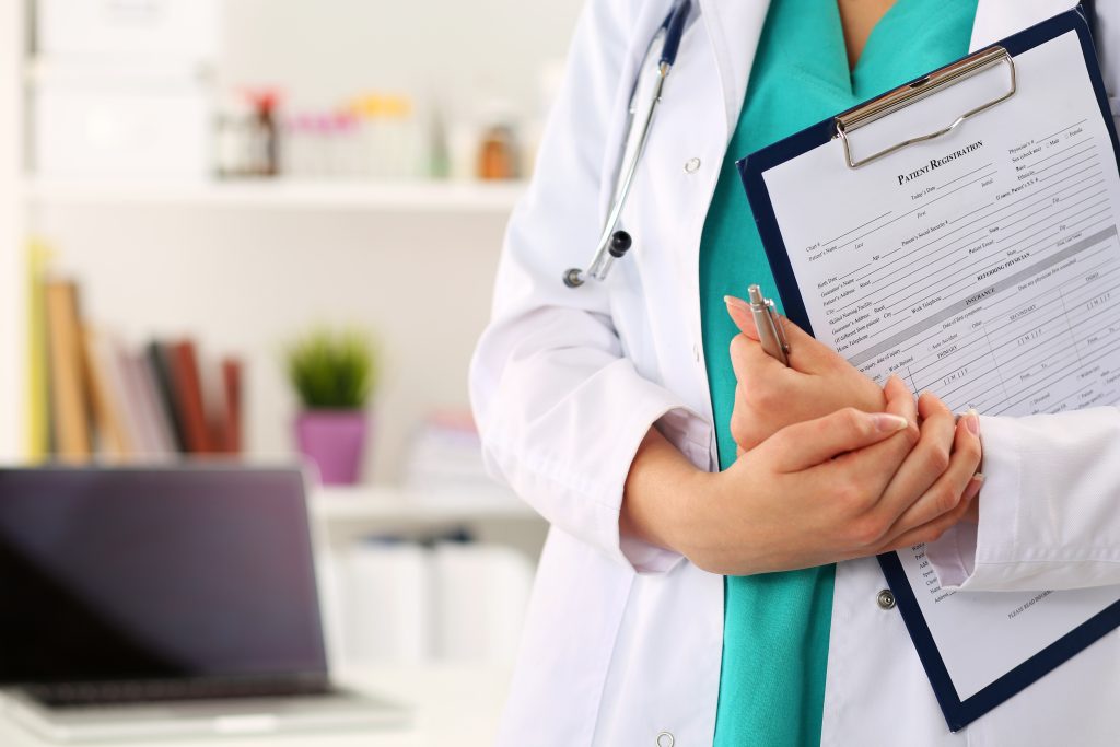 Close up view of female doctor hands holding clipping pad with patient registration form. Healthcare and medical service concept.