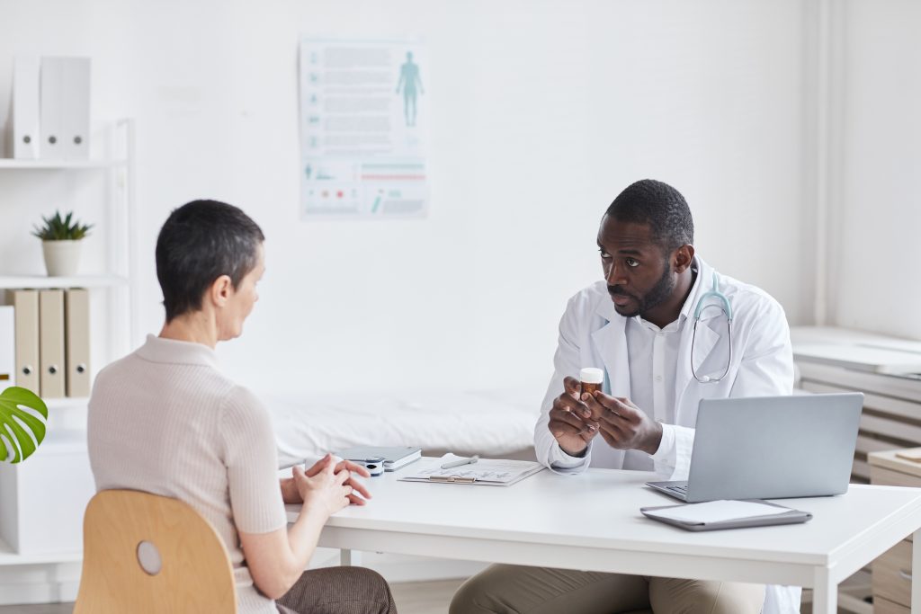 A young doctor sitting at a table in an office, prescribing medicine to a woman patient