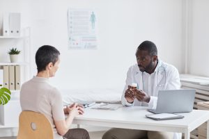 A young doctor sitting at a table in an office, prescribing medicine to a woman patient