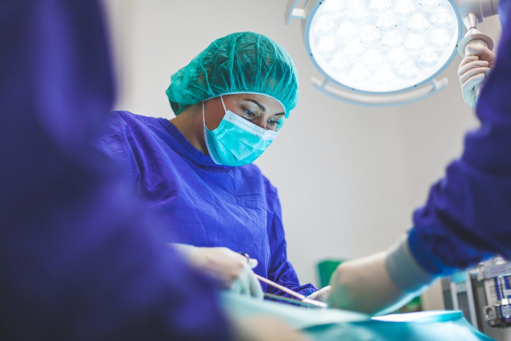 a nurse in scrubs and a mask assists in a medical procedure