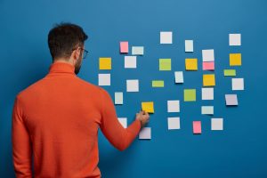 A man organizing his tasks on a blue wall using post-it notes