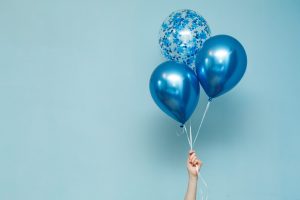 A hand holding a cluster of blue celebratory balloons, creating a joyful and festive atmosphere.