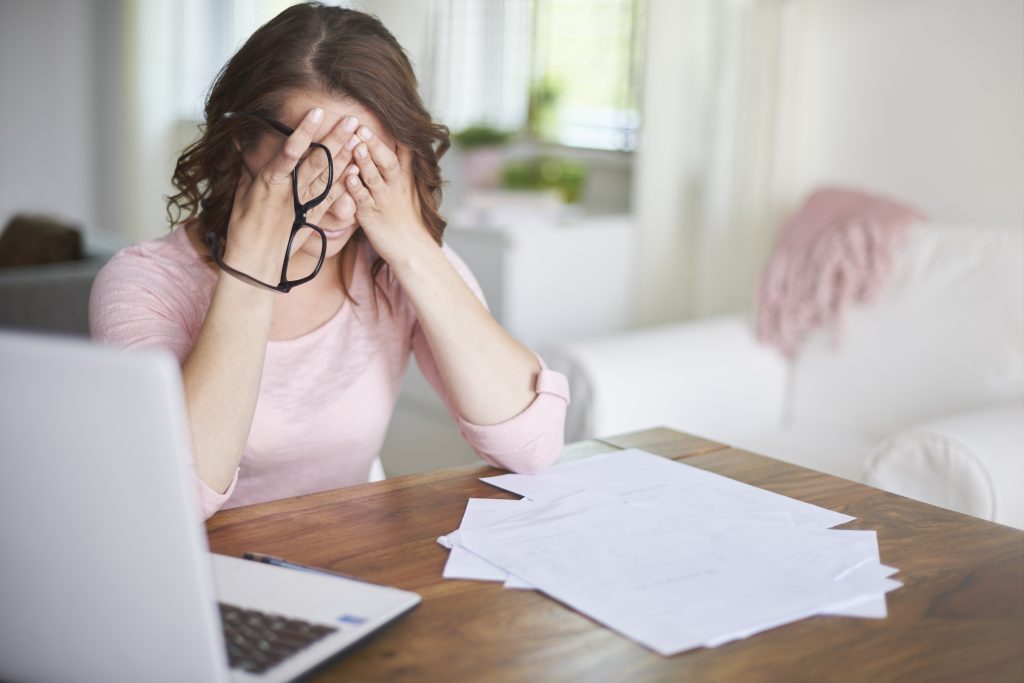 A woman rubs her eyes after looking at paperwork, comparing healthshare options