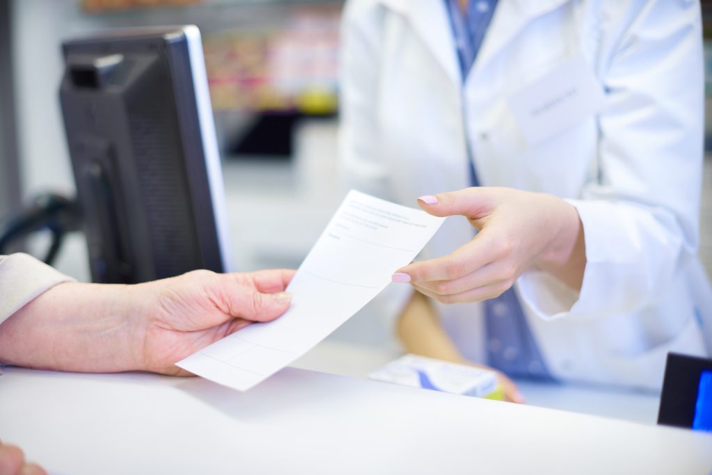 close up of a patient handing a prescription to a pharmacist
