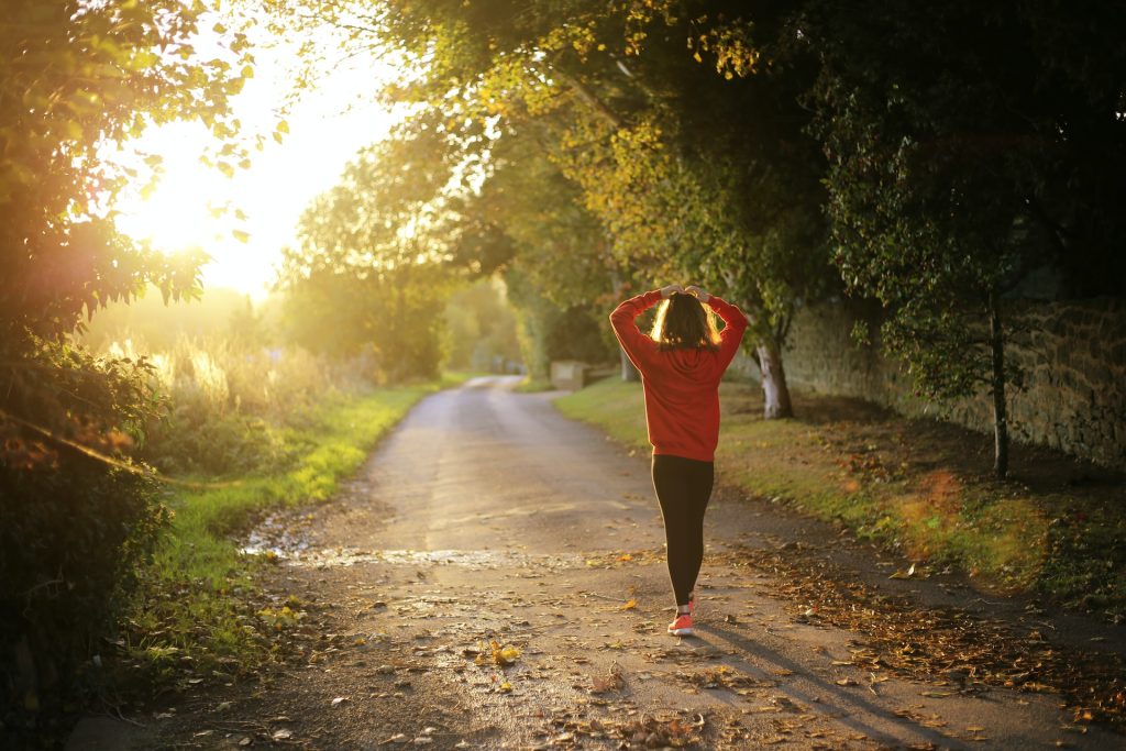 A person walking down a scenic dirt road surrounded by trees, with sunlight streaming through the foliage