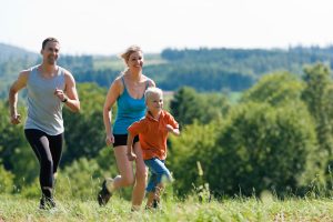 two parents and a child running across a grassy hilltop