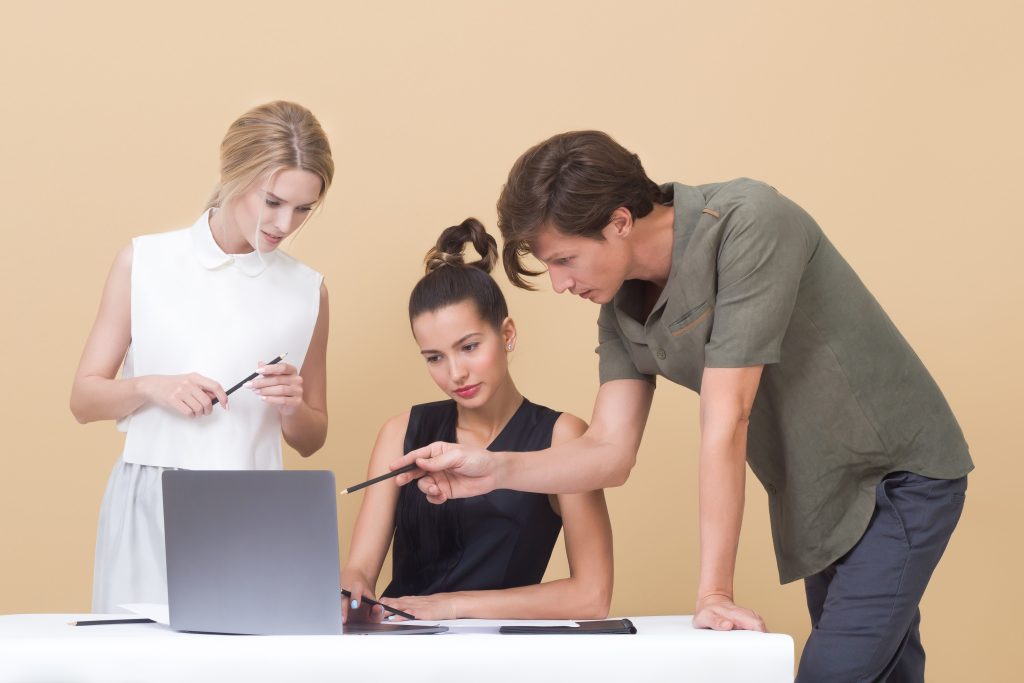 Three people look at a laptop, with one of them pointing at something on the screen.